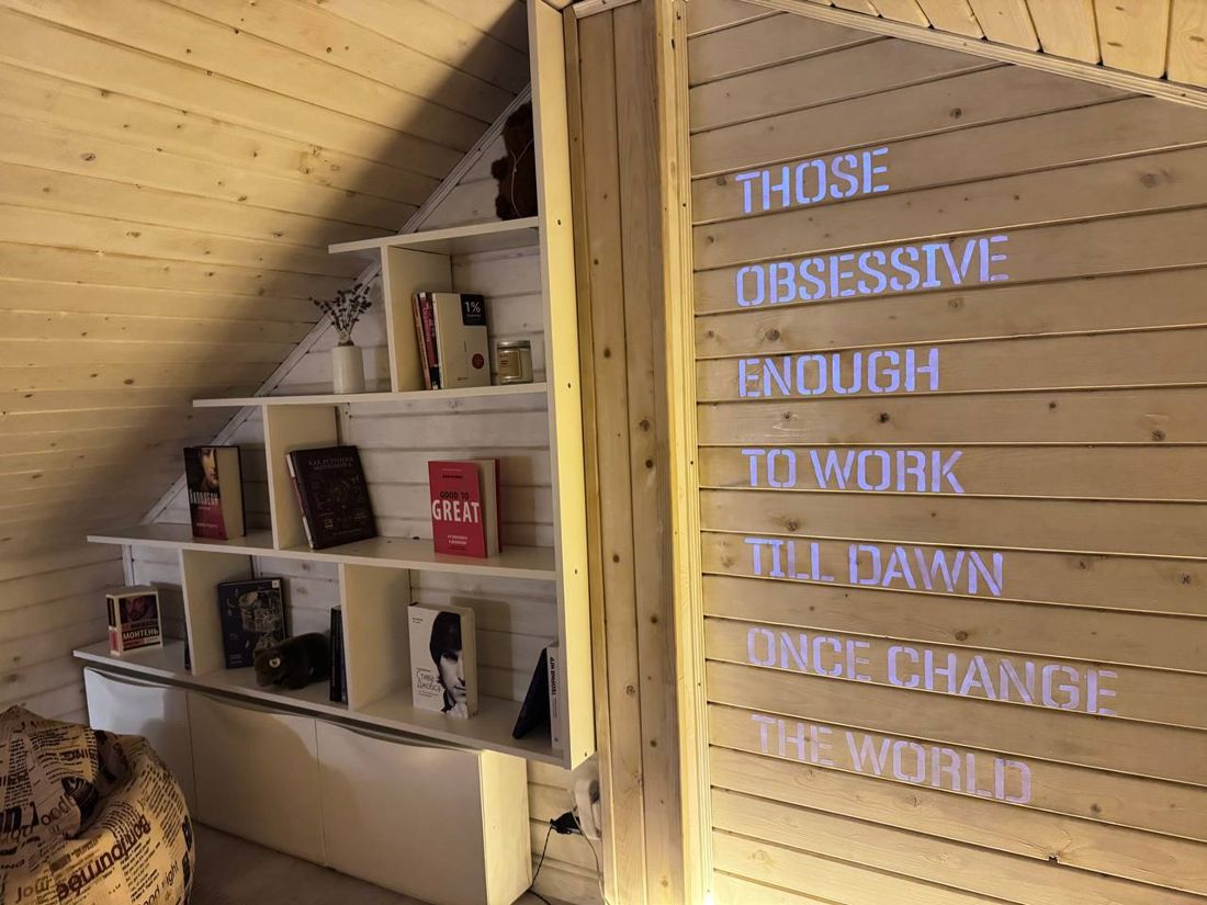 The reading corner: a bookshelf under the slope of the roof and, on the wall, the line those obsessive enough to work till dawn once change the world