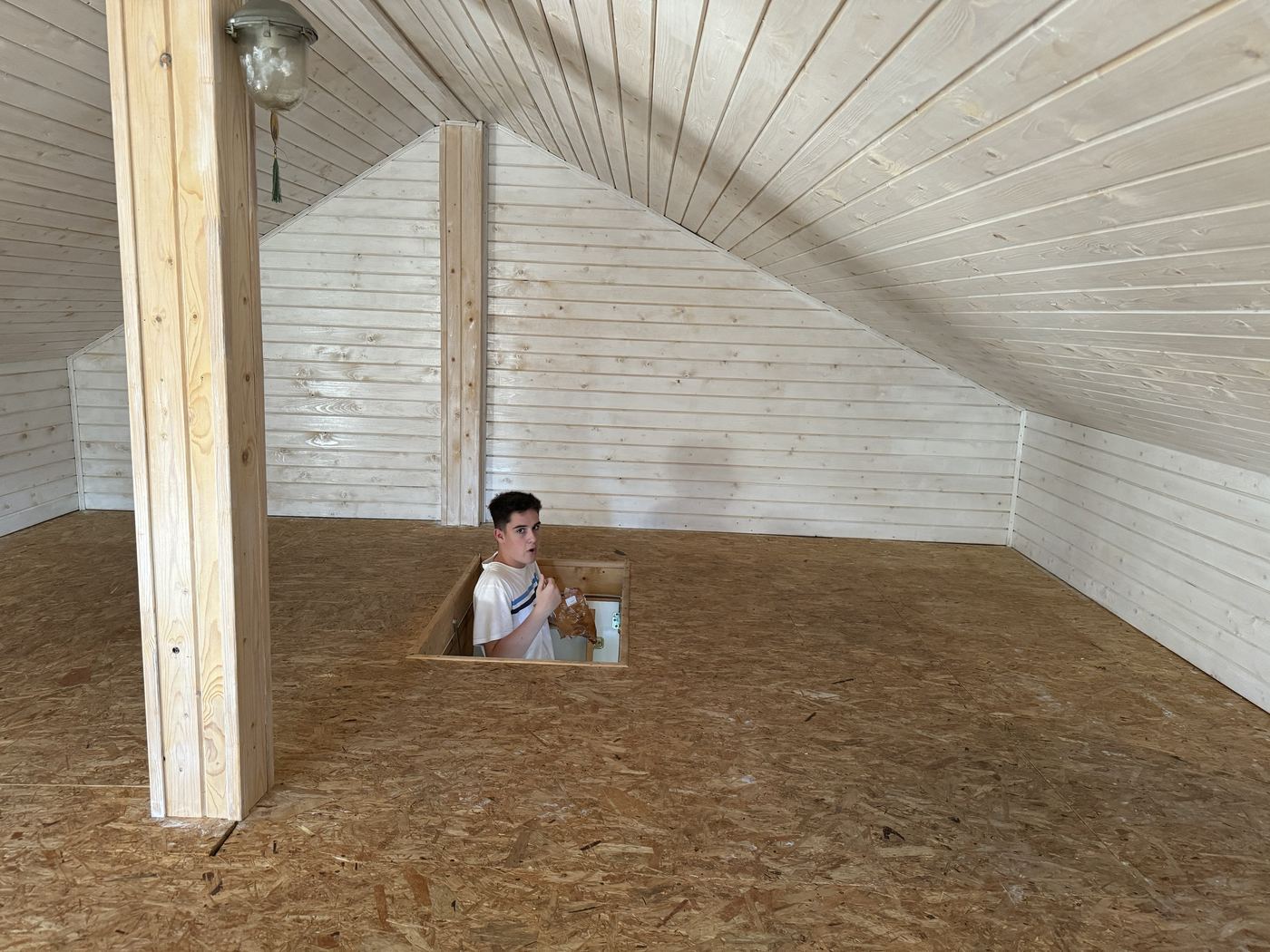 The attic with its walls and ceiling painted white, bare OSB floor, and one of us coming up through the hatch