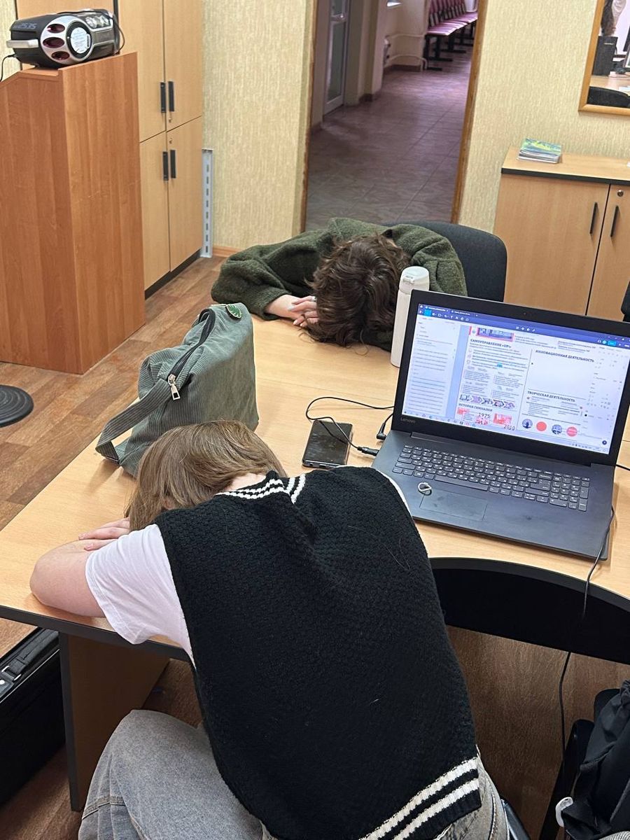 Two members of the media department asleep at a desk next to a laptop with the newspaper layout open