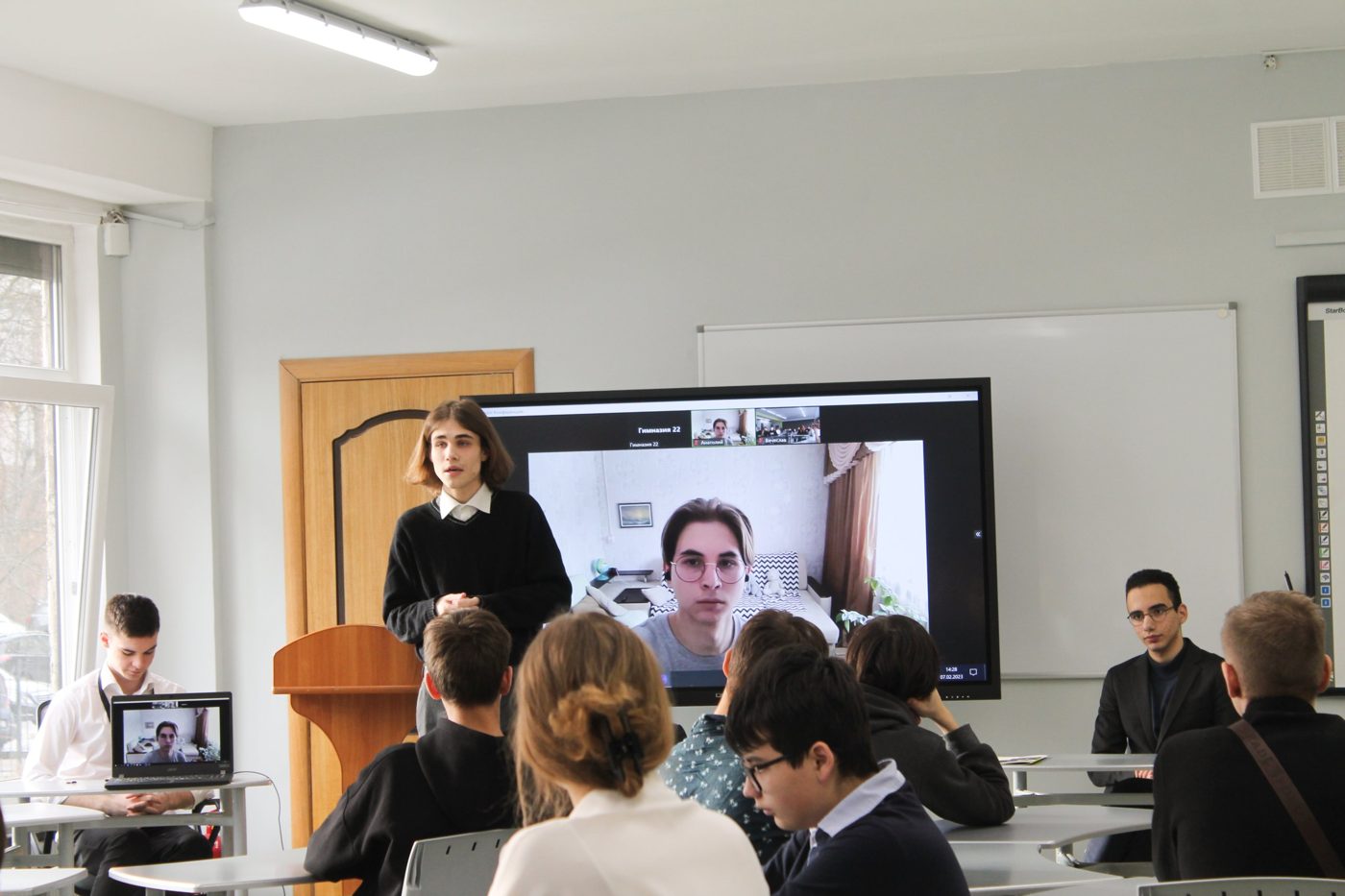 A student speaking at a lectern next to a screen with a video call, at an open meeting with winners of an MGIMO competition