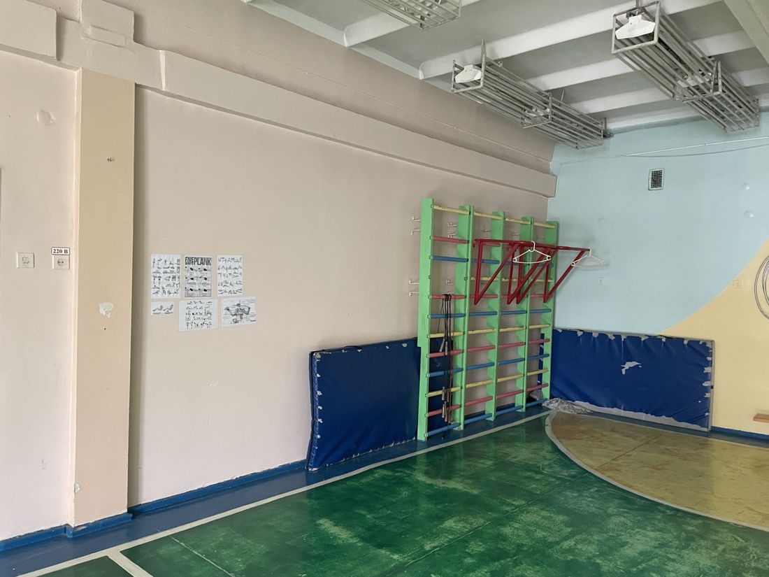 The old gym for the younger classes: bare walls, wall bars and worn blue mats