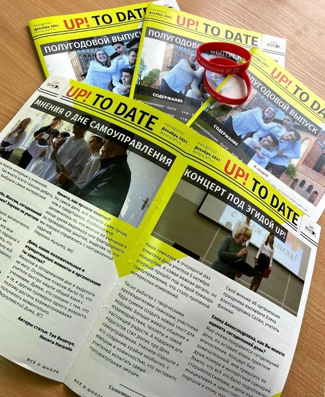 The first printed issues of UP! TO DATE from December 2021 spread on a desk with red gymnasium wristbands
